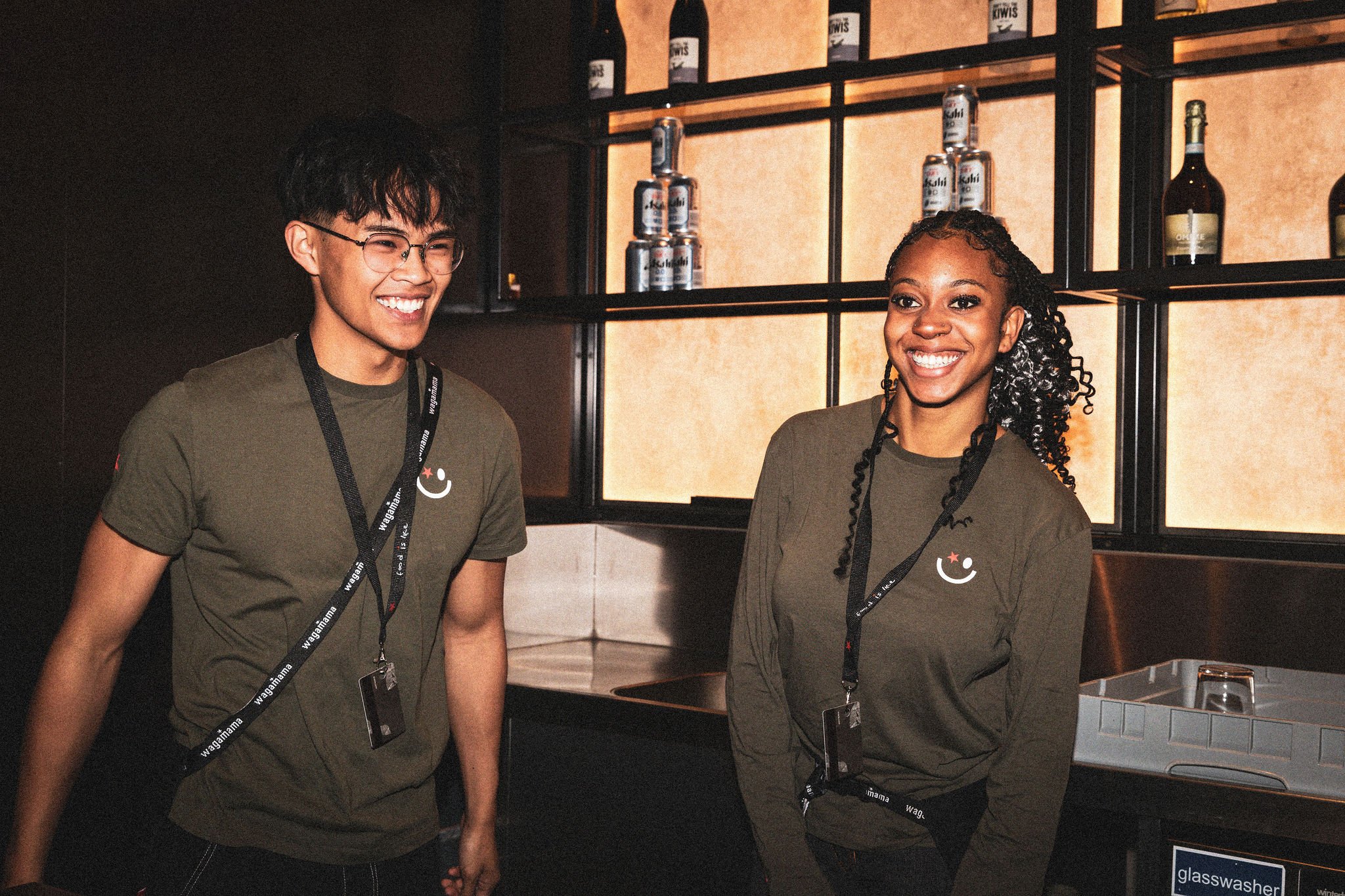 Two employees wearing matching olive green shirts with lanyards.