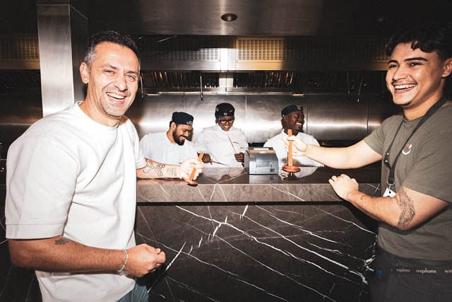 Group of chefs smiling at the camera, holding wooden utensils.