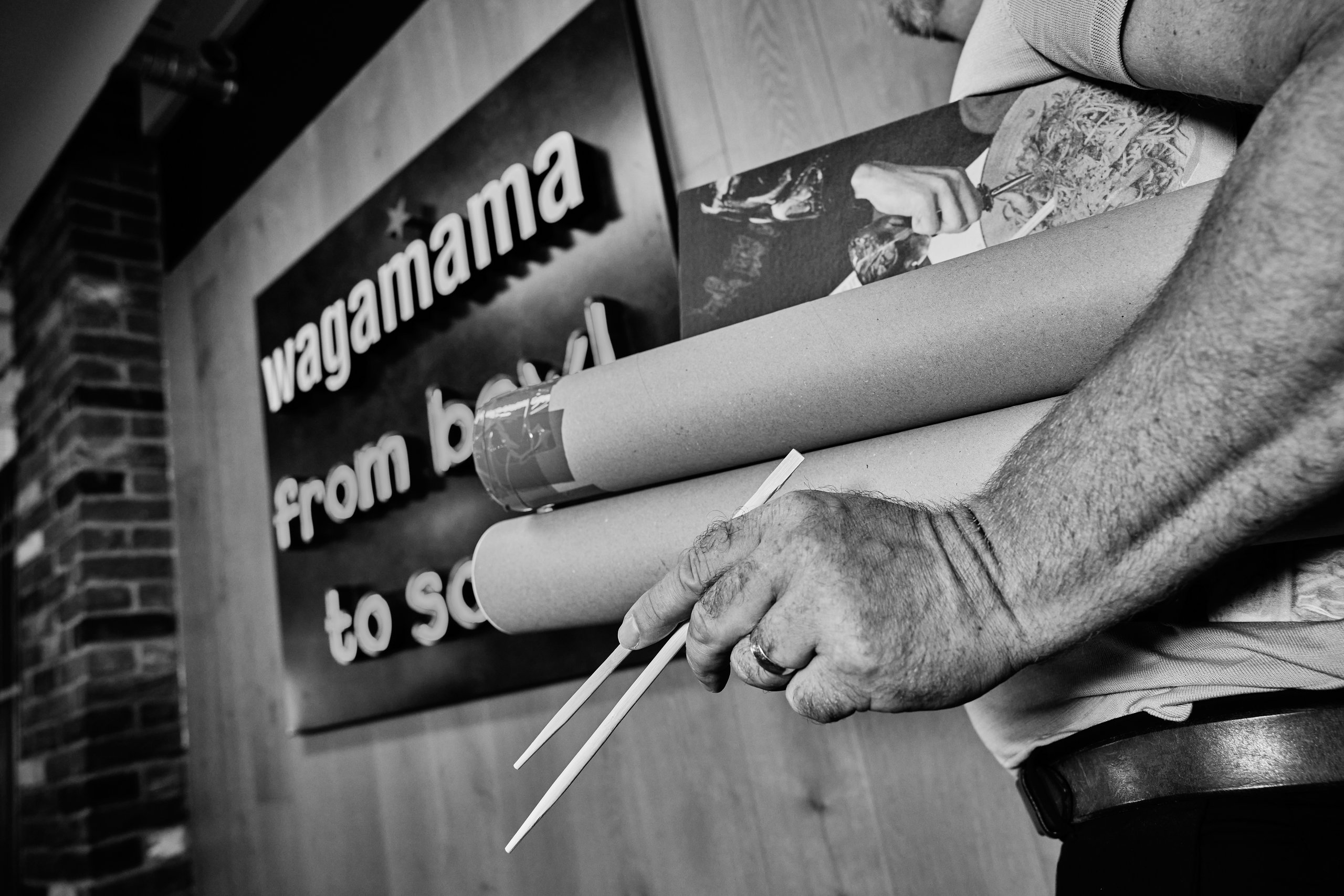 Man holding chopsticks in front of a Wagamama poster.