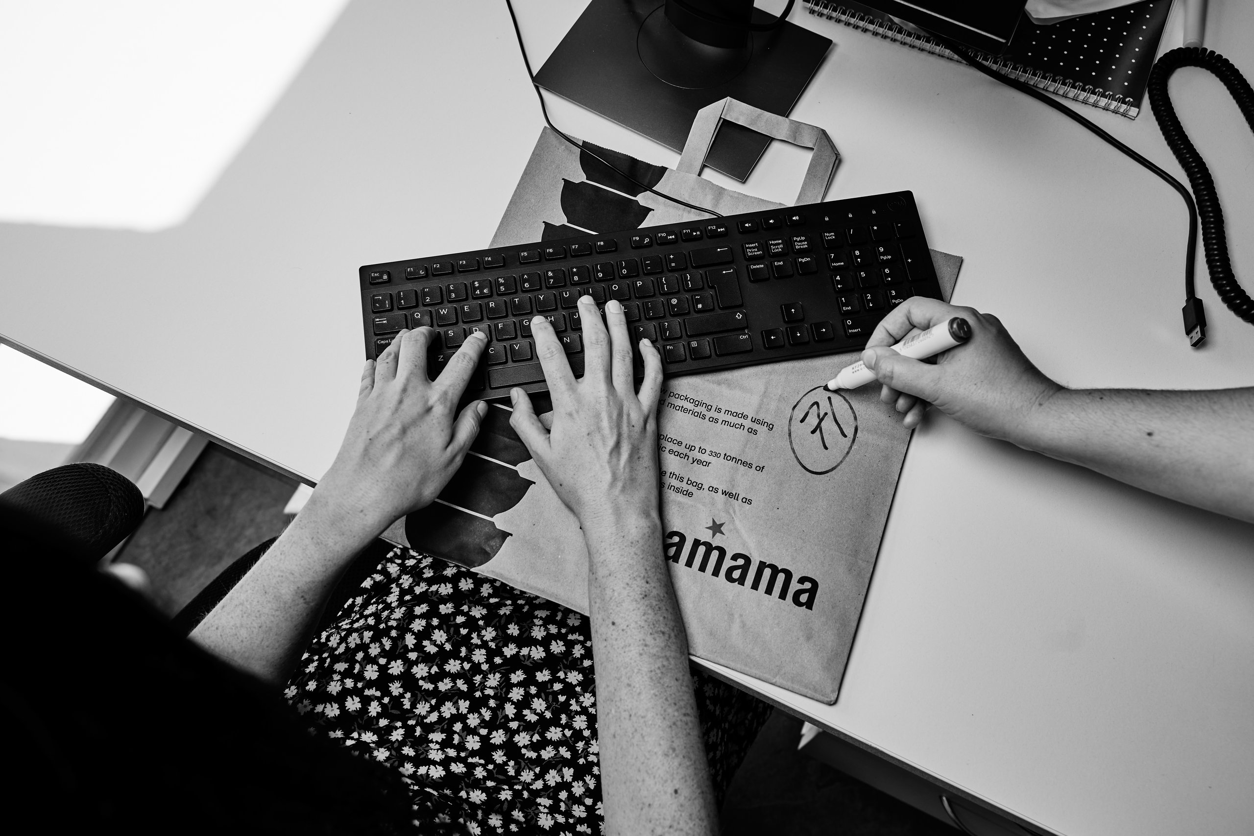 Person typing on keyboard, drawing on paper. Office setup.