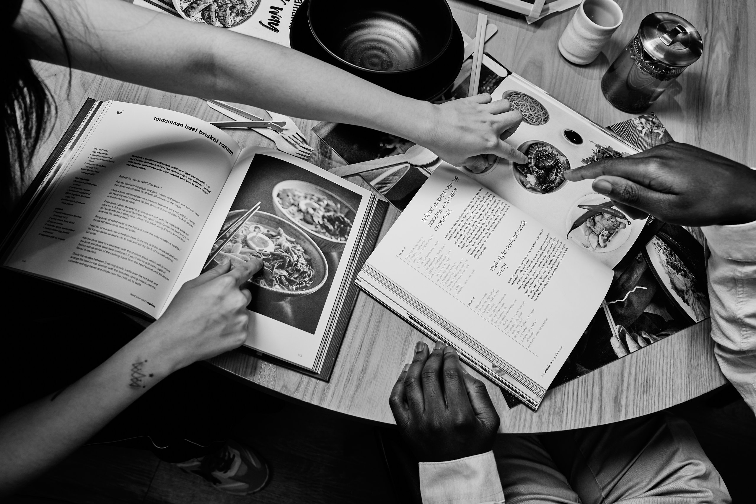People pointing at a cookbook with recipes.