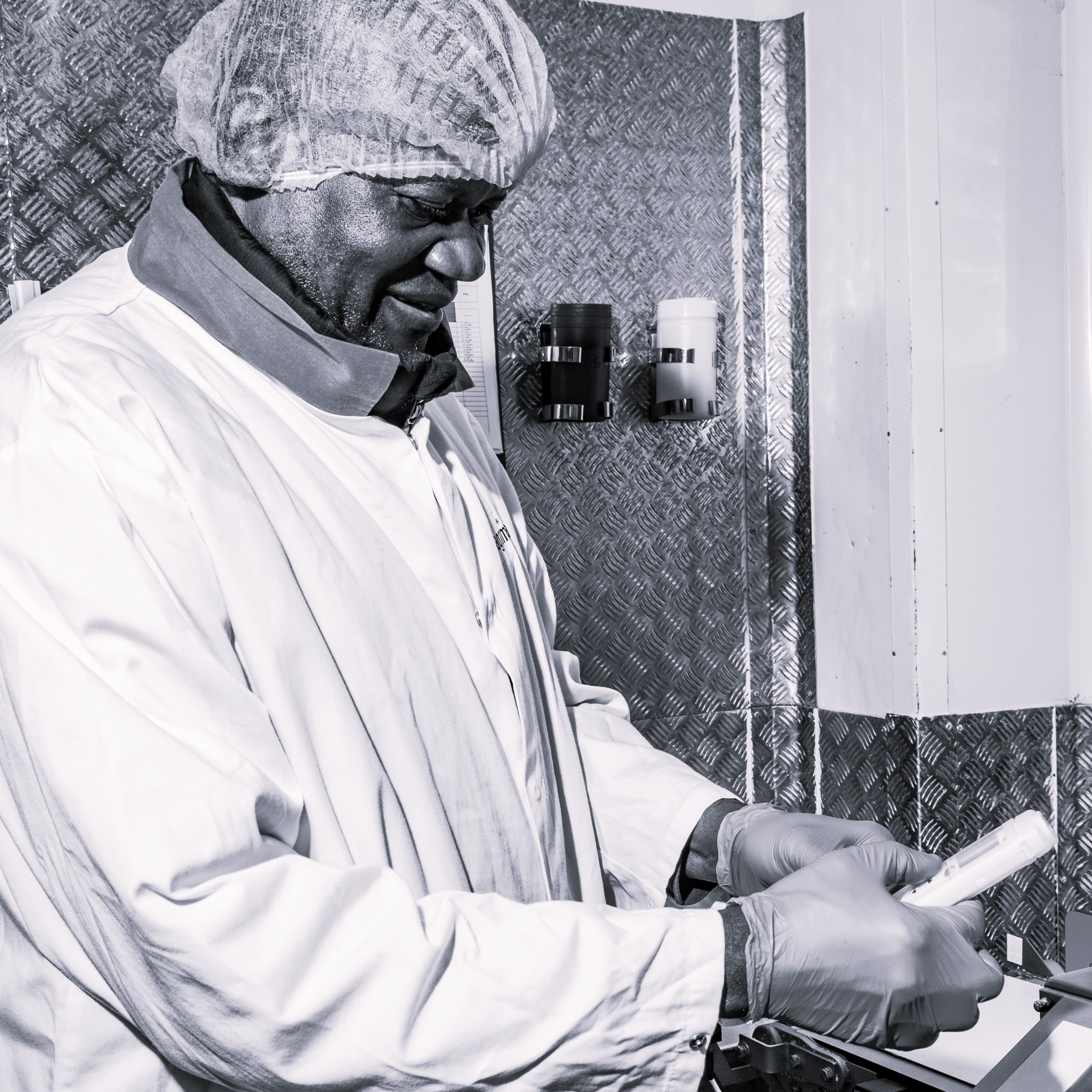 Man in gloves, hair net, and lab coat is working.