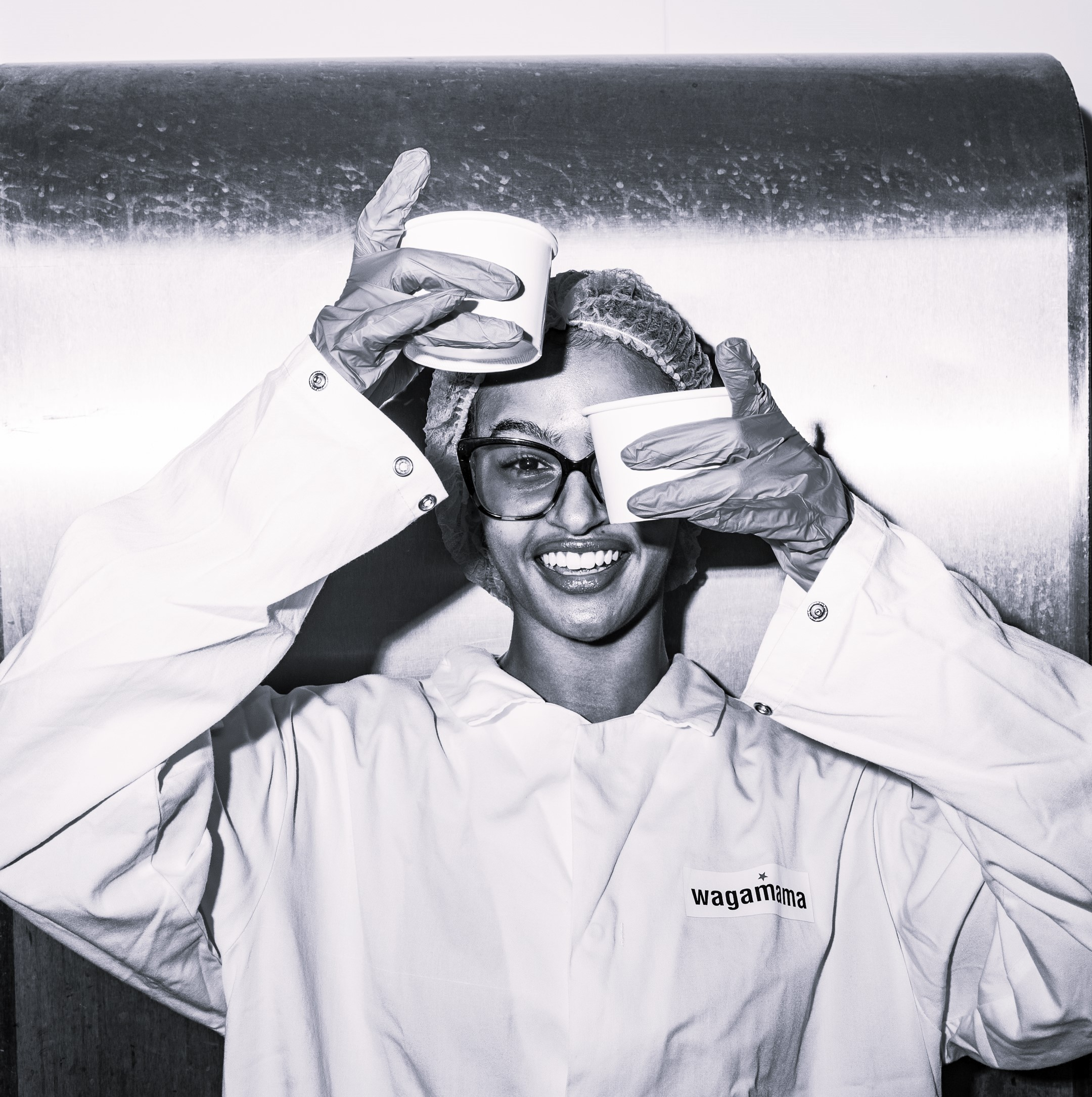 Woman in a uniform holding cups, wearing glasses, and smiling.