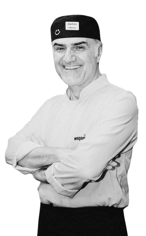 A smiling male chef in a Wagamama uniform with arms crossed, isolated against a white background.