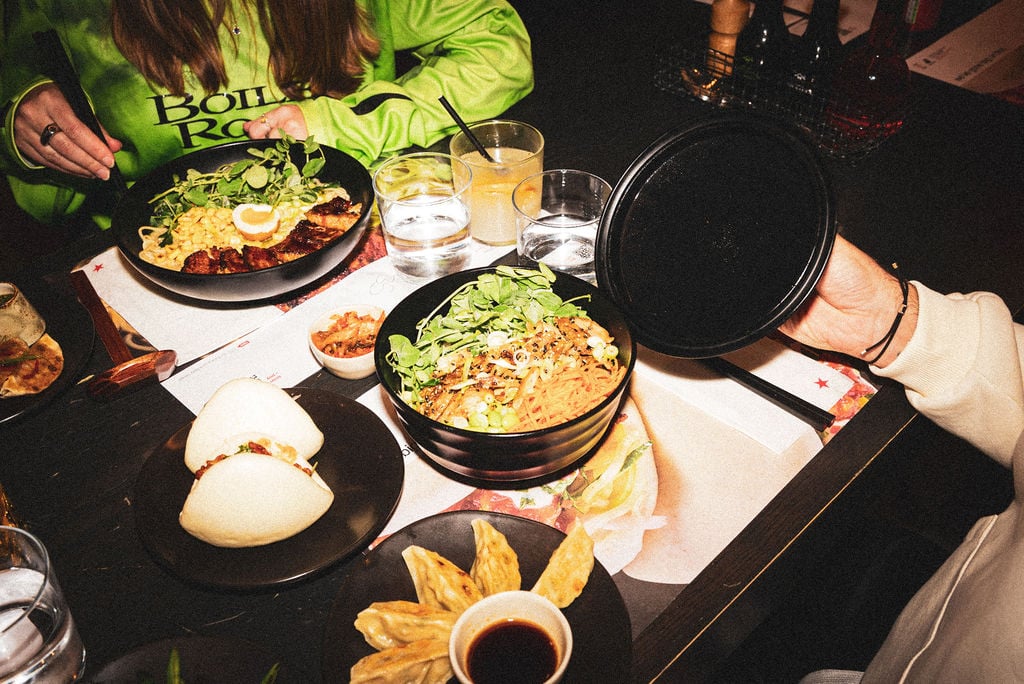 A table spread with ramen, bao buns, and gyoza at a restaurant setting.