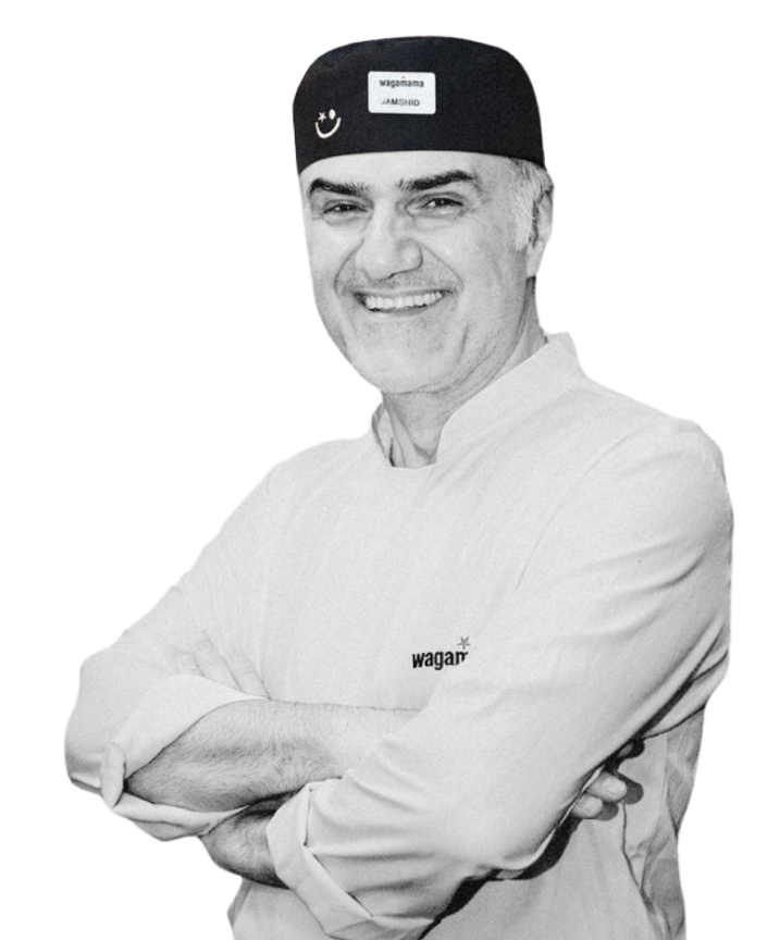 A smiling chef wearing a black Wagamama uniform and cap, posing with arms crossed.