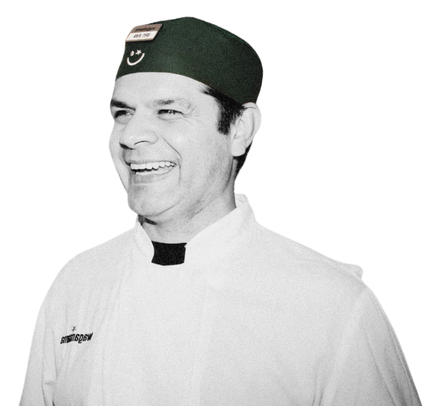 A smiling chef wearing a dark green cap and white uniform, shot against a white background.