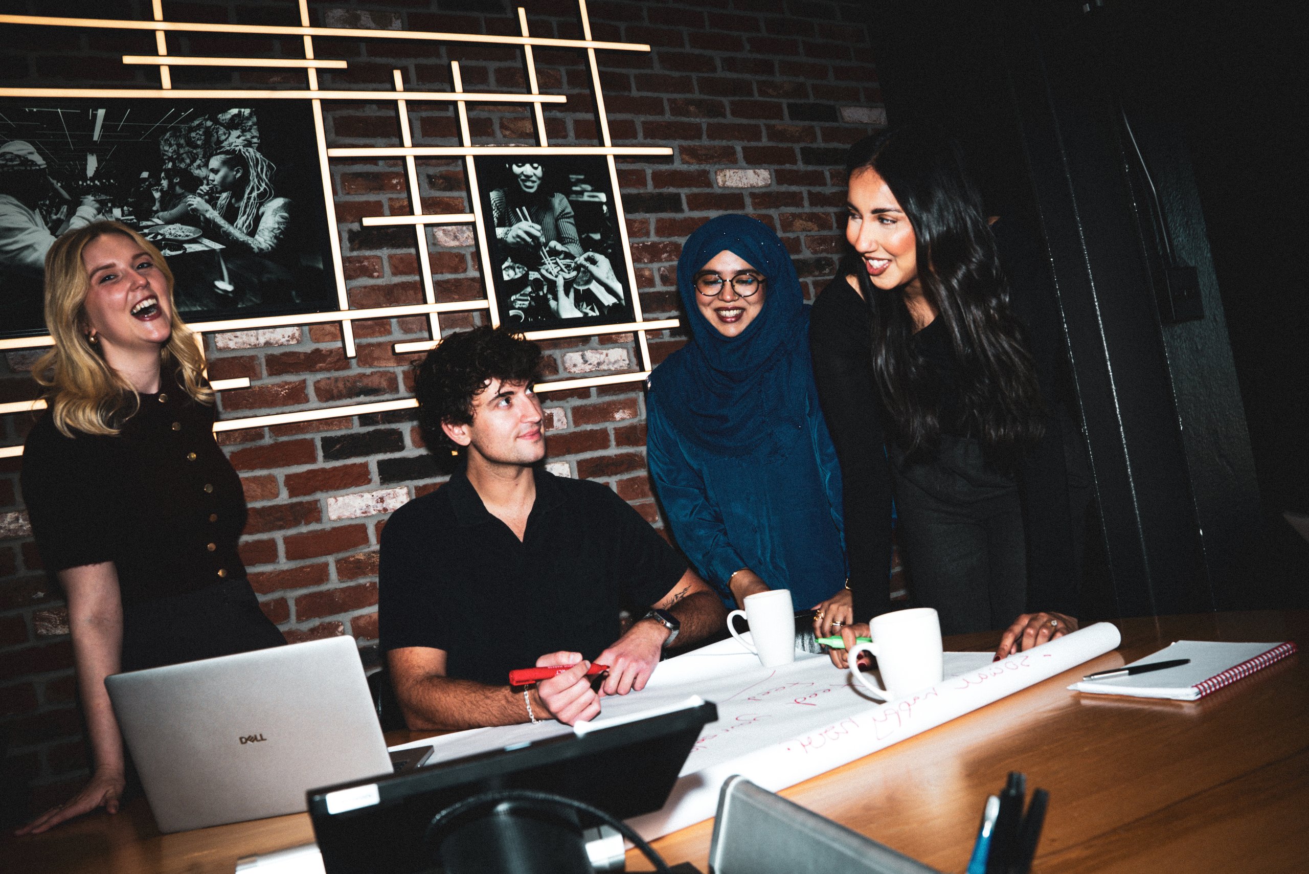 A diverse group of four young professionals laughing while collaborating on a project at a table.