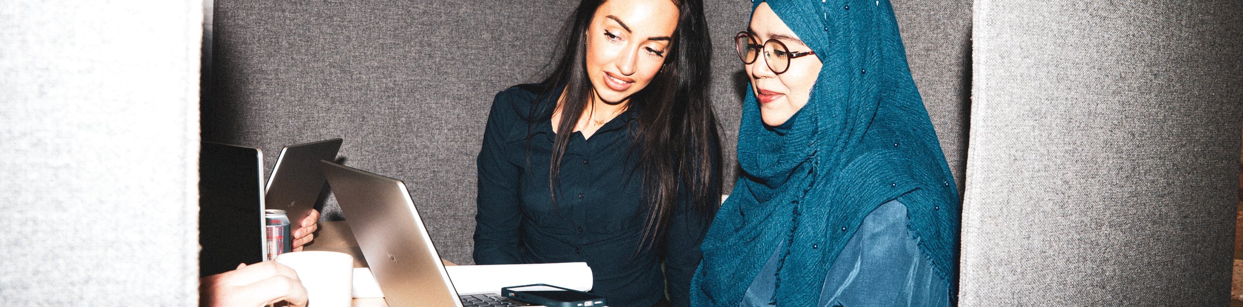 Two women collaborating on a laptop at a small table inside a private, high-backed office booth.