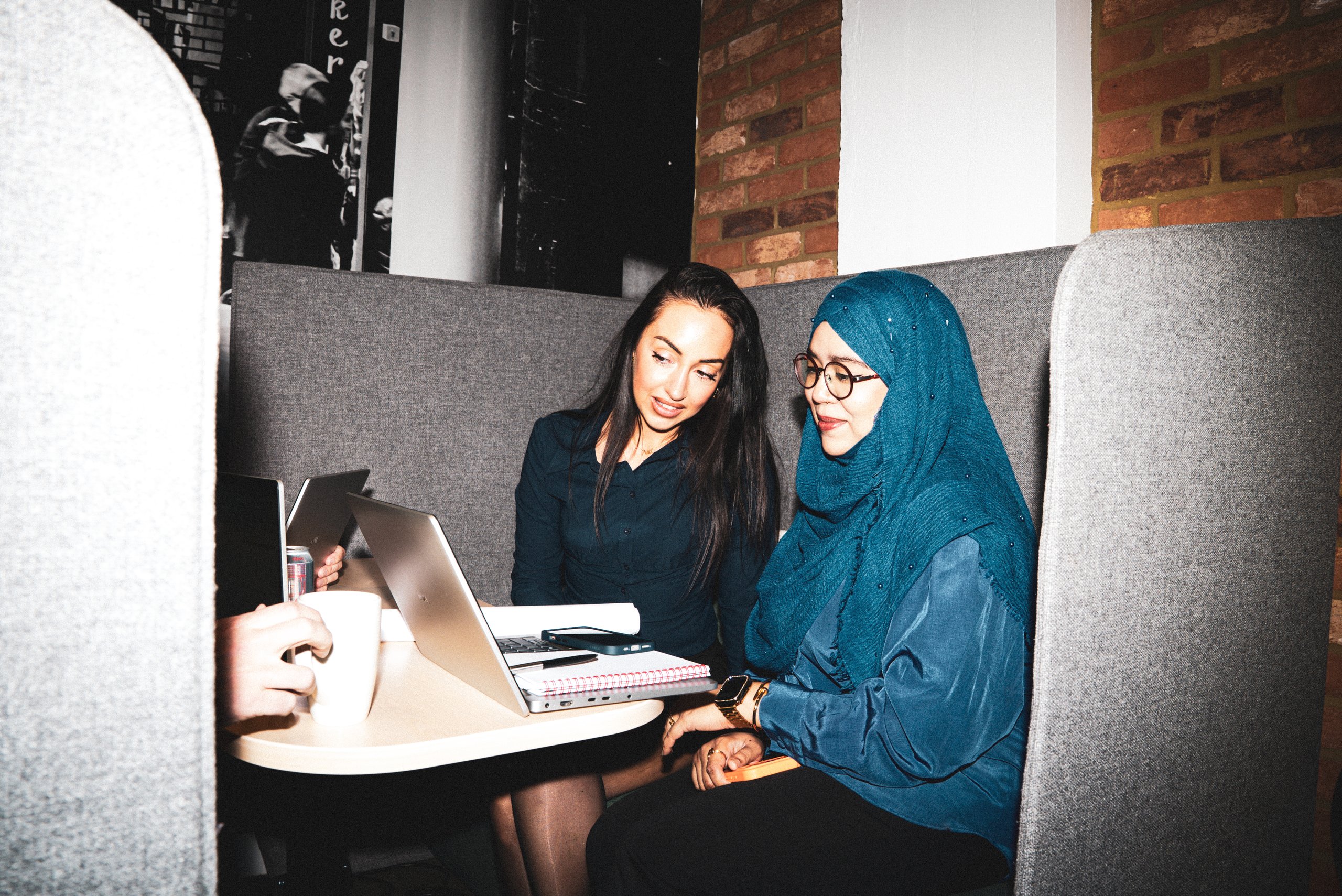 Two women collaborating on a laptop at a small table inside a private, high-backed office booth.