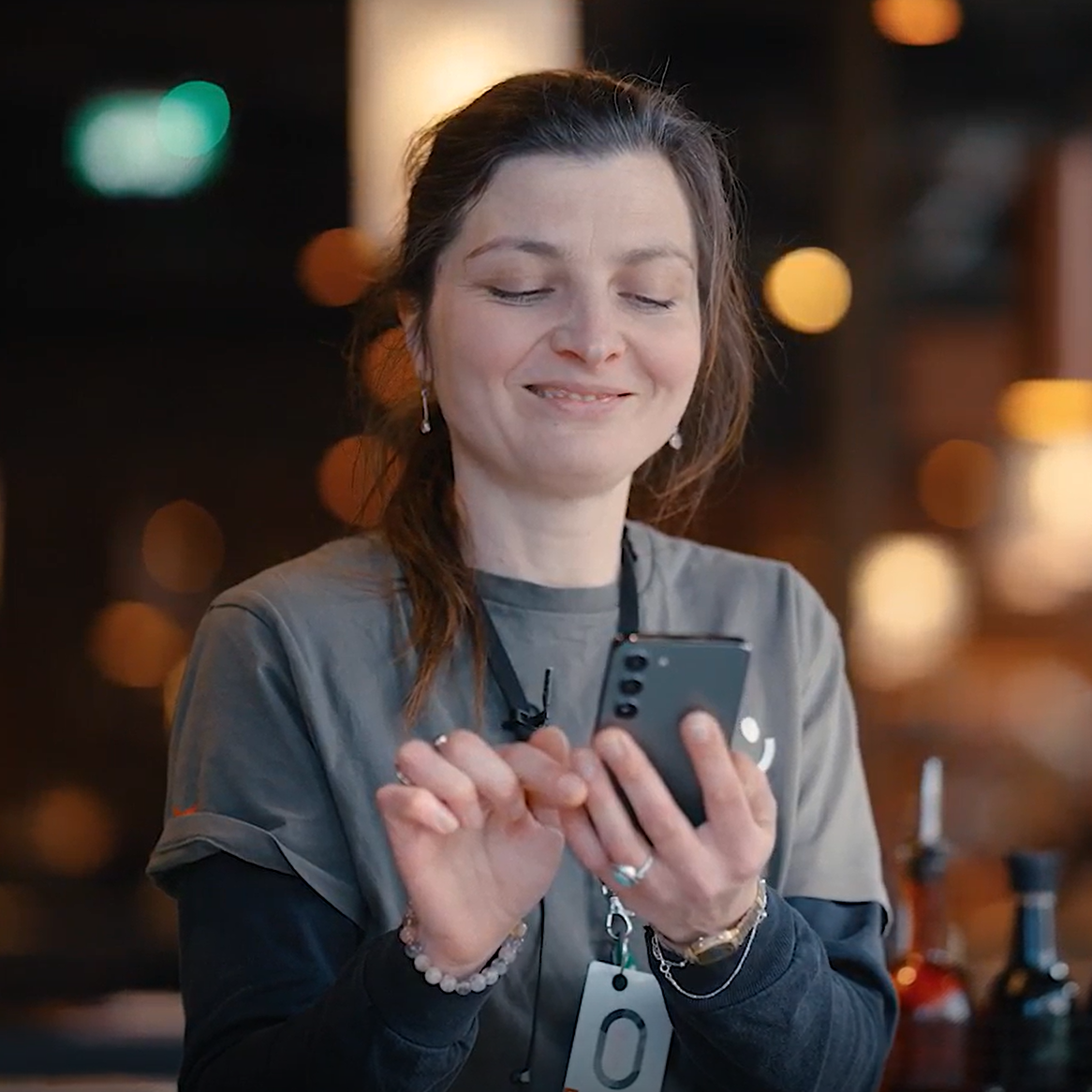 A smiling woman wearing a grey t-shirt looking at and tapping on her smartphone.