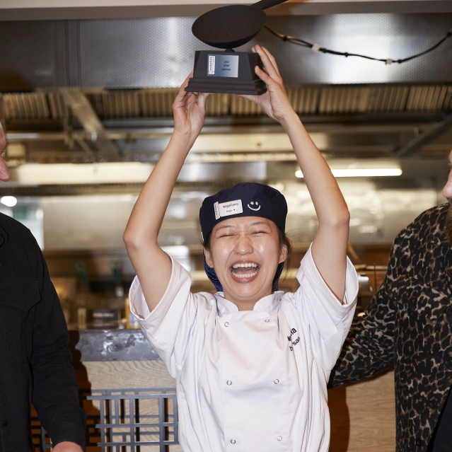 A jubilant chef in a Wagamama uniform lifts a ladle-shaped award high above her head.