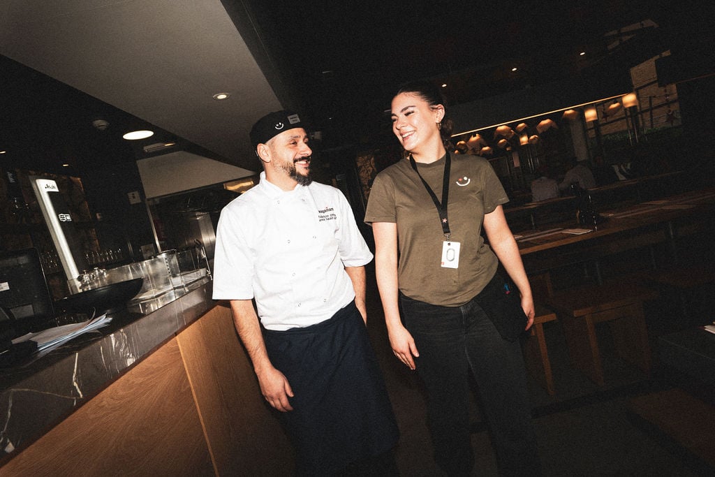 A chef and a female restaurant staff member smiling and walking together in a modern eatery.