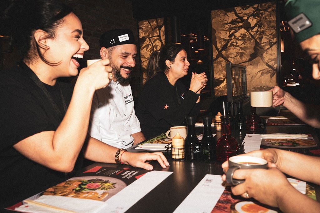 Restaurant staff members sitting at a table together laughing and drinking from mugs.